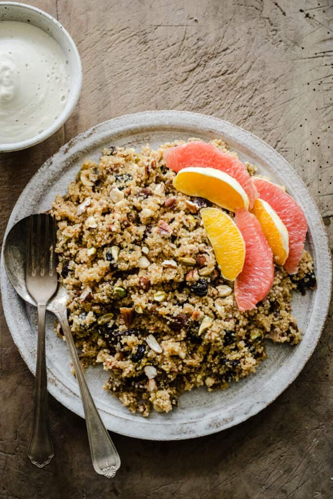 Breakfast Quinoa on a plate with citrus fruits next to a bowl of cashew cream