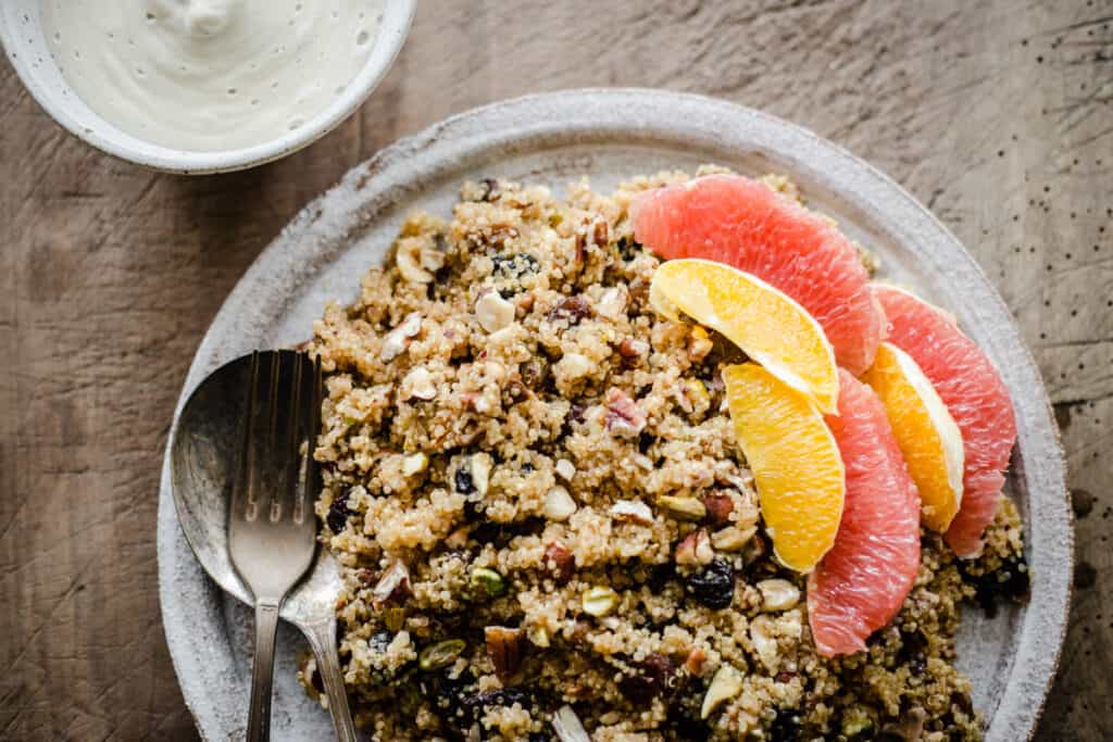 Breakfast Quinoa on a plate with citrus fruits next to a bowl of cashew cream