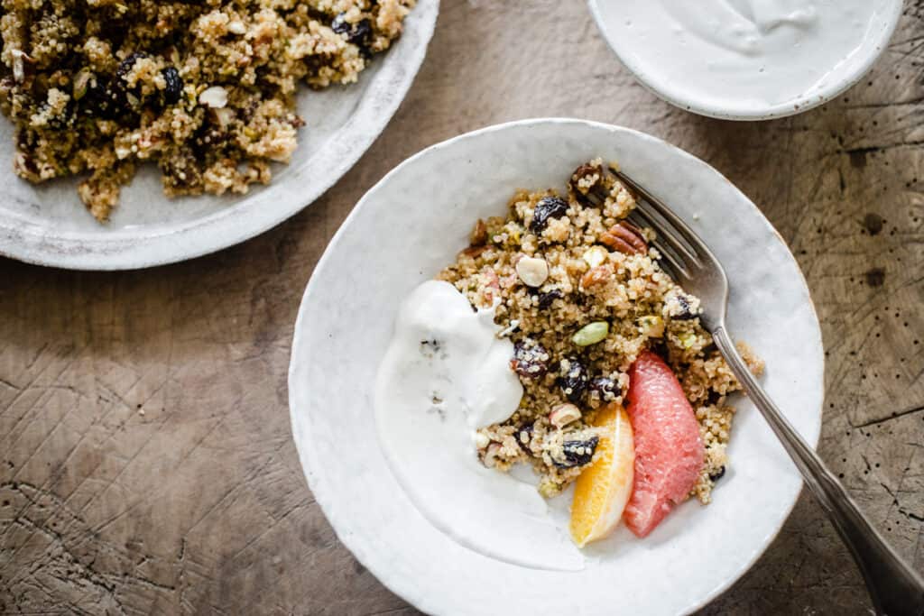 A bowl of Breakfast Quinoa with cashew cream and citrus fruits on a wooden board