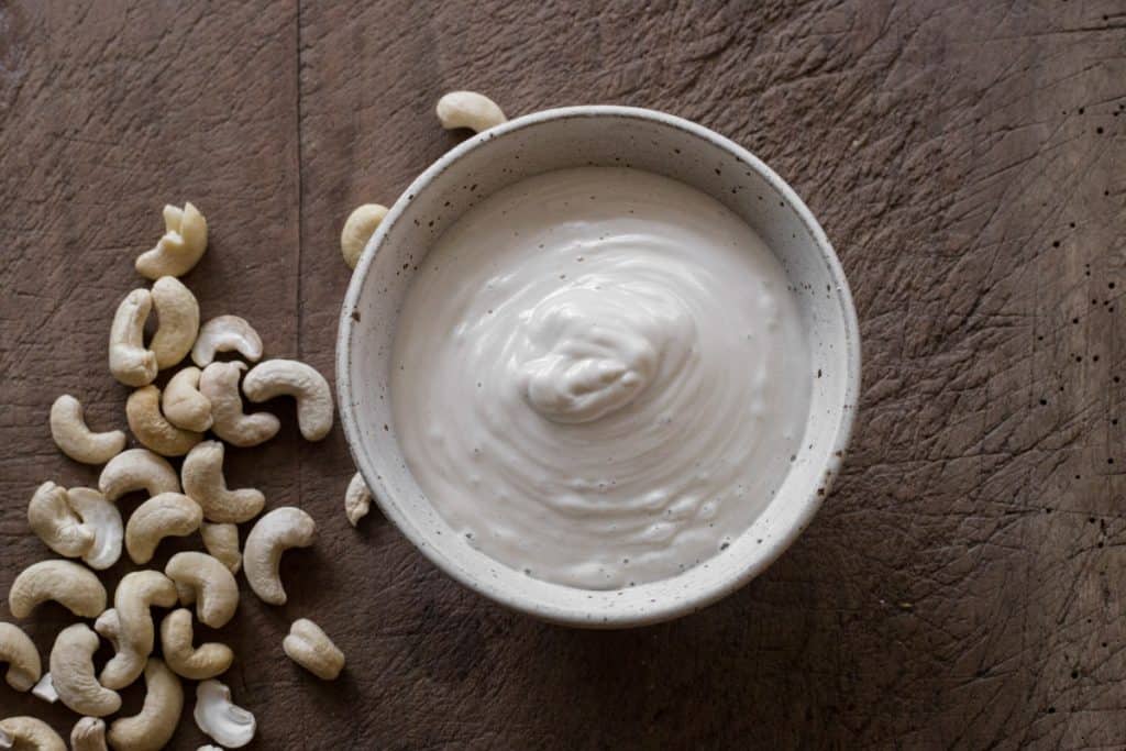 Bowl of cashew cream next to cashews on a wooden board