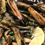 Roasted Aubergine and Courgette with Sumac and Herbs in a baking tray with a wedge of lemon