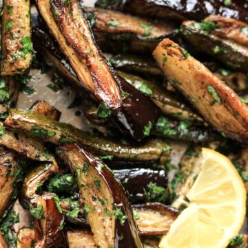 Roasted Aubergine and Courgette with Sumac and Herbs in a baking tray with a wedge of lemon