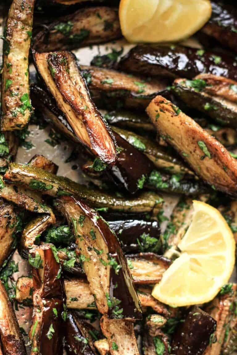 Roasted Aubergine and Courgette with Sumac and Herbs in a baking tray with a wedge of lemon