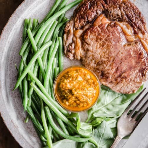 Steak with green beans and sun-dried tomato sauce on a white plate