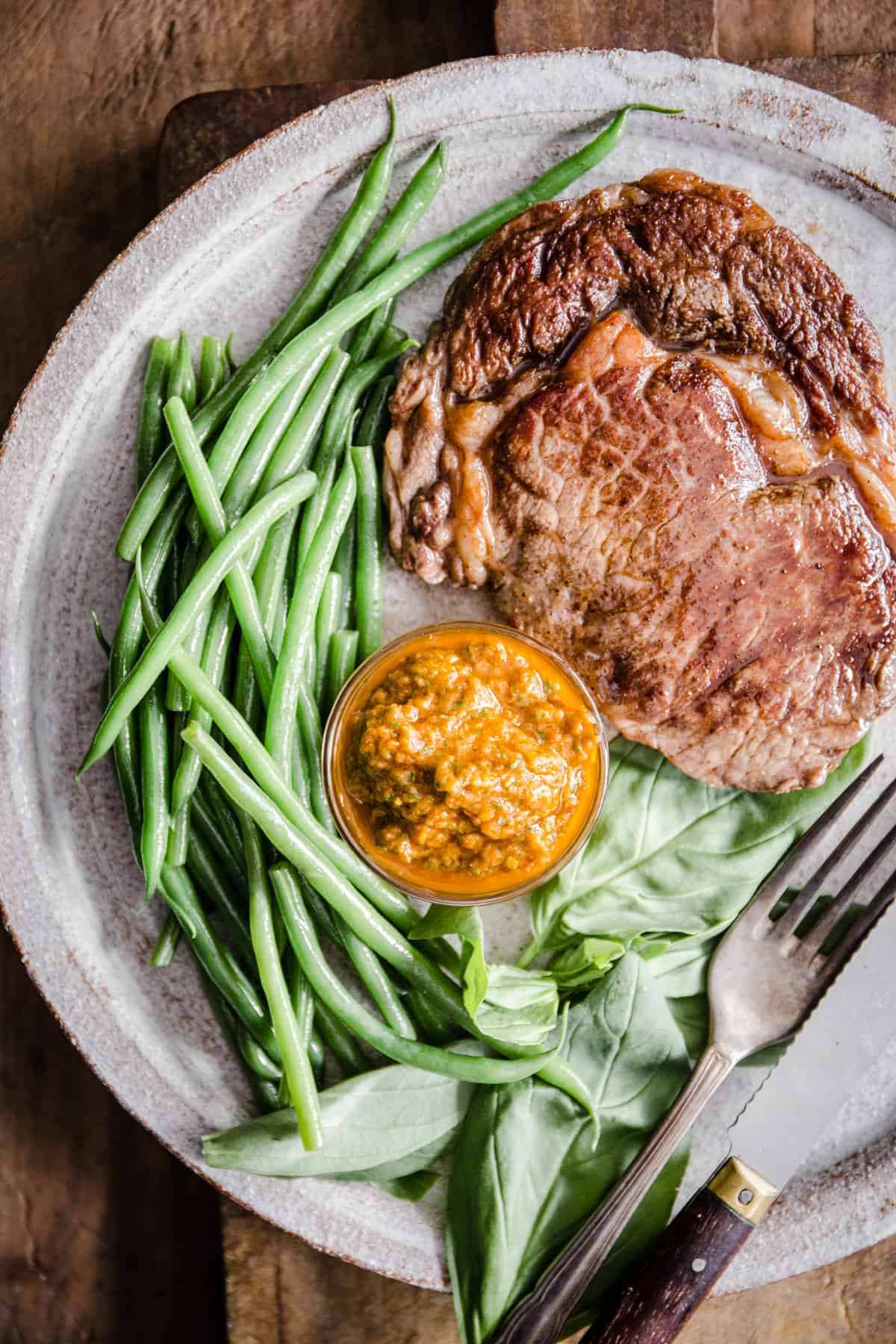 Steak with green beans and sun-dried tomato sauce on a white plate