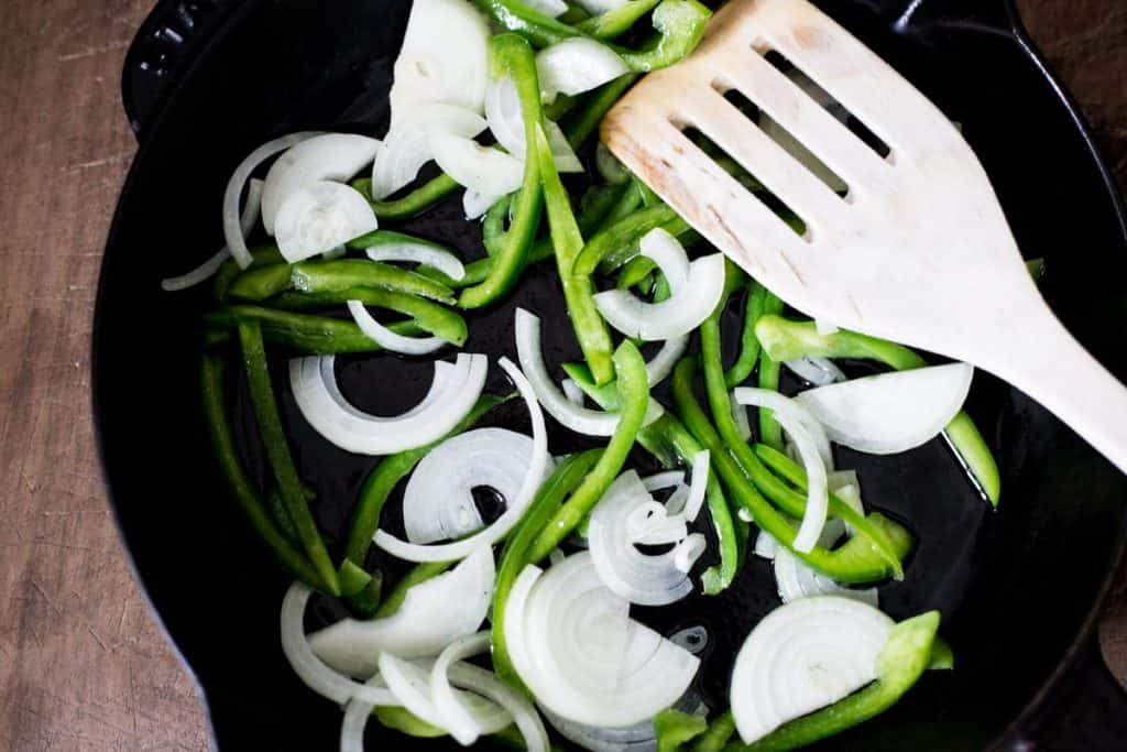 Sliced green peppers and onions in a cast iron skillet