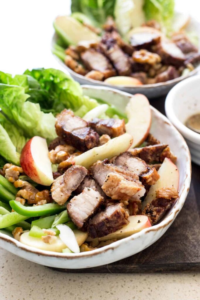 Roast Pork Belly Apple & Caramelised Walnut Salad in a white bowl on a wooden board