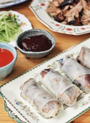 A plate of summer rolls sitting on top of a wooden table next to hoisin sauce
