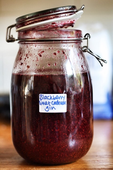 A glass jar of blackberry gin sitting on top of a wooden table