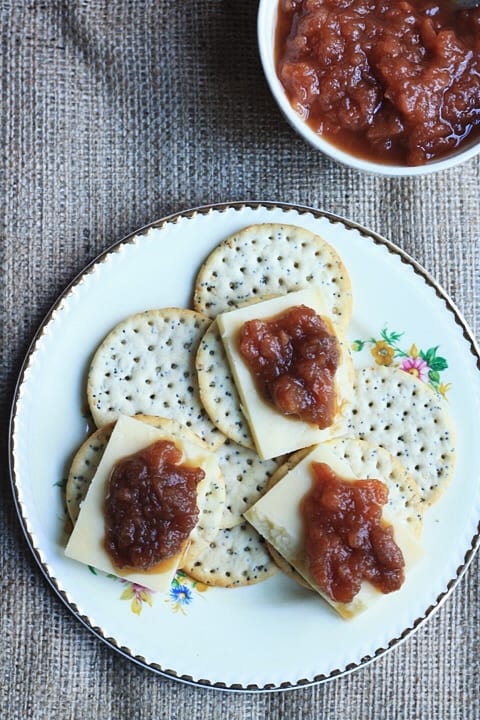 A close up of cheese and chutney on crackers on a plate on a table