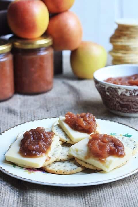 A close up of cheese and chutney on crackers on a plate on a table