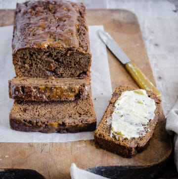 GF Malt Loaf sliced on a wooden board. Once slice spread with butter.