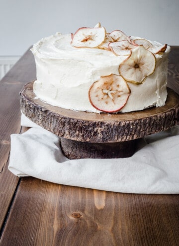 Apple and Cinnamon Cake with Salted Caramel Cream Cheese Buttercream on a cake stand on a wooden table.