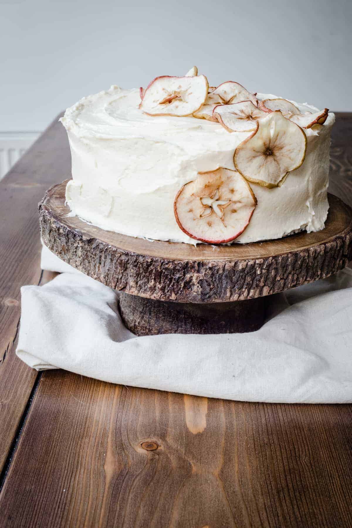 Cinnamon Apple Cake with Salted Caramel Cream Cheese Buttercream on a cake stand on a wooden table.