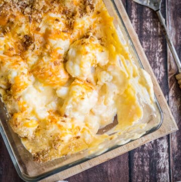 Gluten-Free Cauliflower Cheese in a serving dish with a spoon on a wooden board
