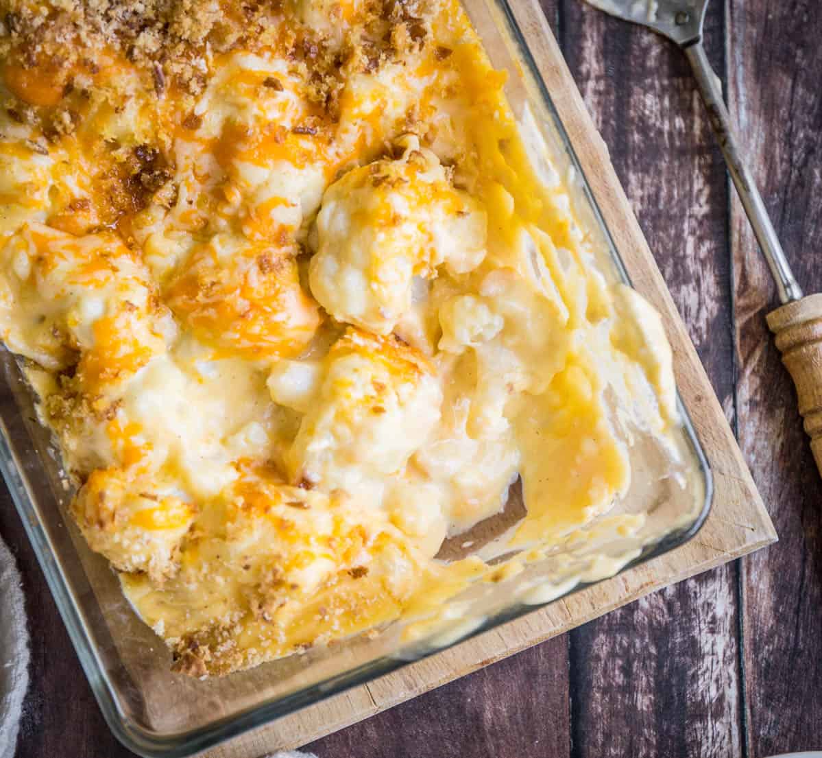 Gluten-Free Cauliflower Cheese in a serving dish with a spoon on a wooden board