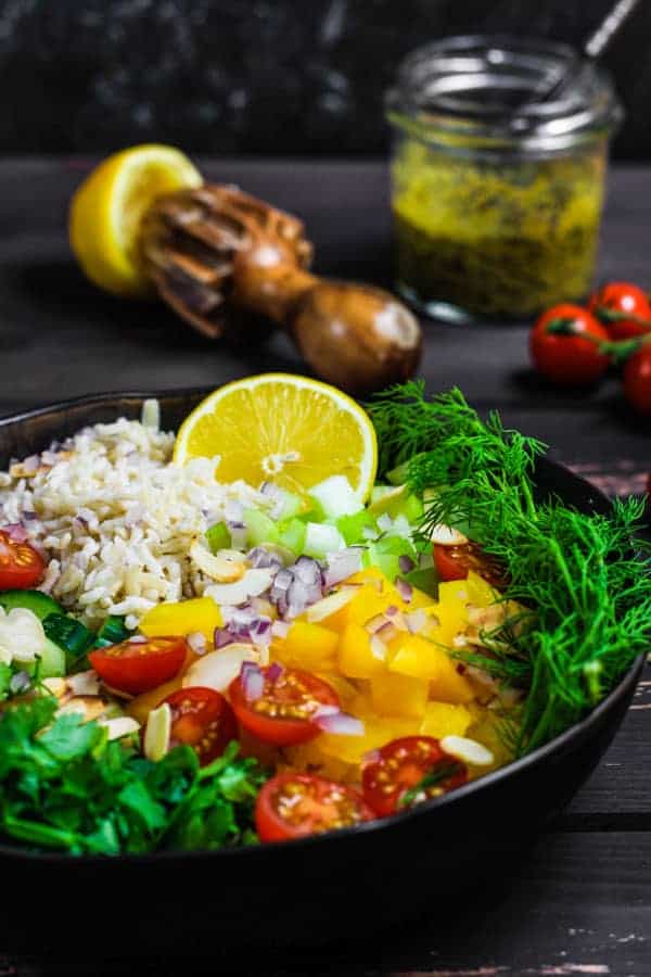 bowl of rice salad ingredients with lemon squeezer, vinaigrette and tomatoes in background