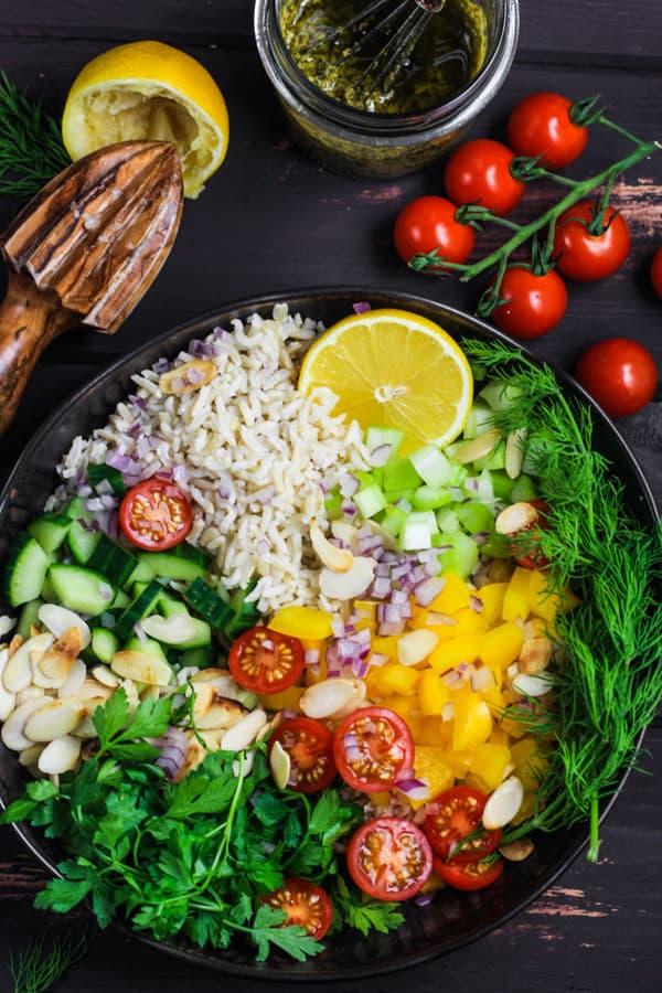 bowl of rice salad ingredients with lemon squeezer, vinaigrette and tomatoes in background