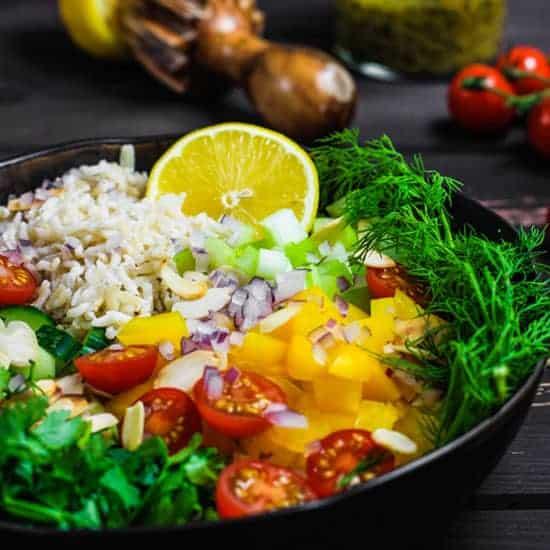 Simple Brown Rice Salad with Pesto Vinaigrette bowl of rice salad ingredients with lemon squeezer, vinaigrette and tomatoes in background