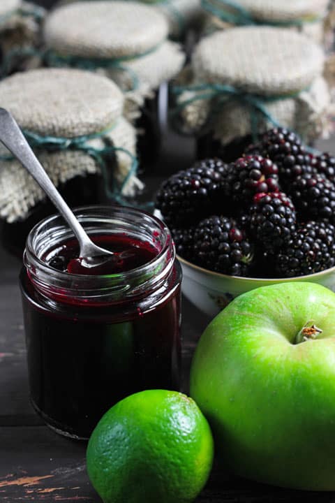 A jar of blackberry jam next to blackberries and apples