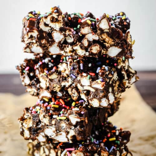 side view of stack of Ultimate Popcorn Rocky Road bars on baking parchment on wooden board