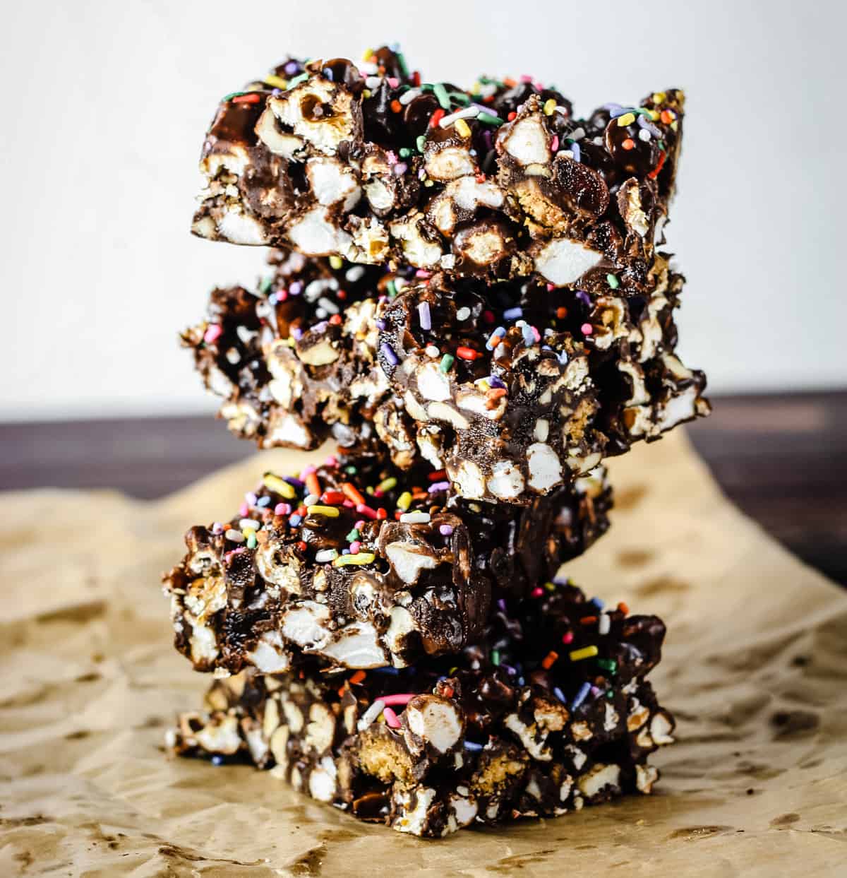 side view of stack of Ultimate Popcorn Rocky Road bars on baking parchment on wooden board