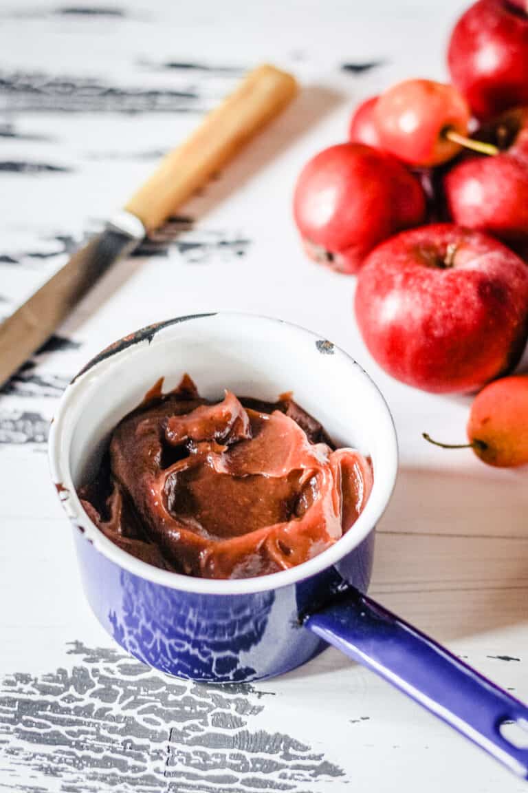 A dish of apple butter on a white table next to apples.