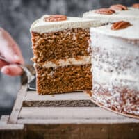 Hand pulling out a slice of Pecan Butterscotch Latte from whole cake on a wooden box