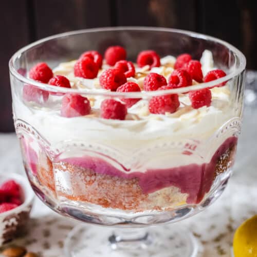 A large glass bowl of trifle on a table topped with raspberries