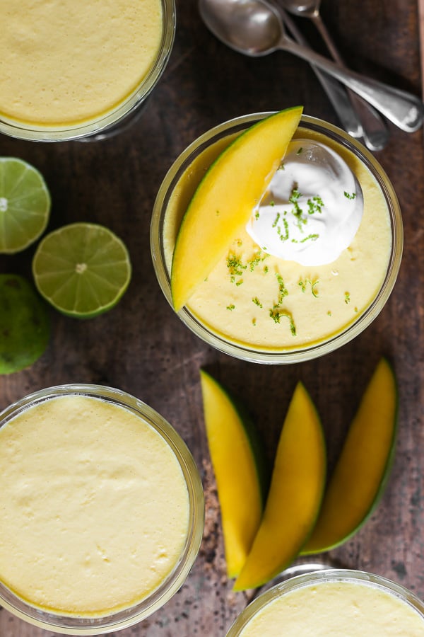 glass bowls of mango pudding on a wooden table next to limes