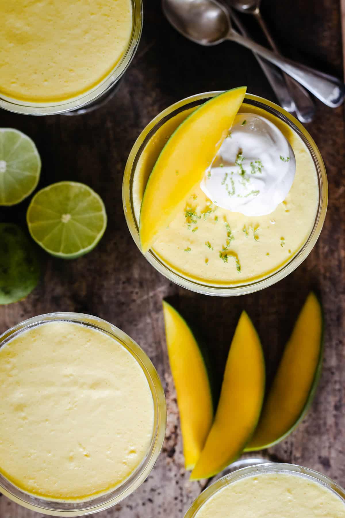 glass bowls of mango pudding on a wooden table next to limes