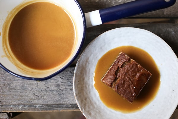 sticky toffee pudding in a bowl next to pan of toffee sauce