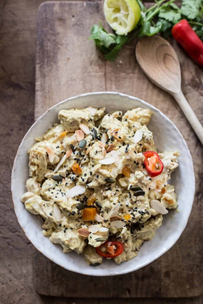 A bowl of coronation chicken on a wooden board