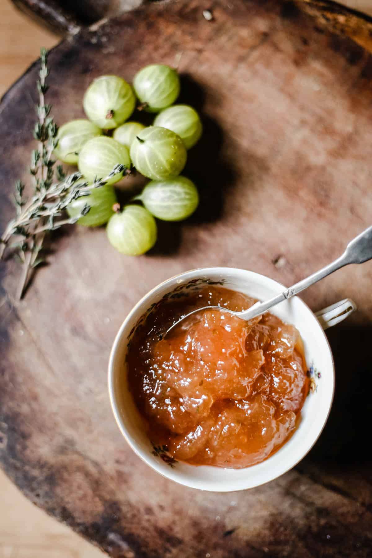 Overhead image of Gooseberry Thyme Jam on a wooden board with gooseberries and a sprig of thyme