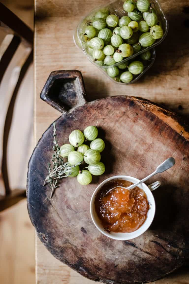 Overhead image of Gooseberry Thyme Jam on a wooden board with gooseberries and a sprig of thyme