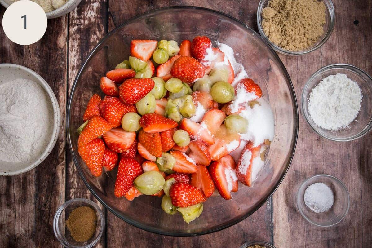 Caster sugar tossed with gooseberries and strawberries in a large mixing bowl.