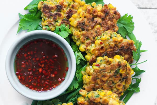 A plate of sweetcorn fritters on a table next to dipping sauce