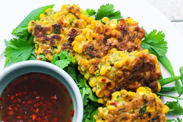 A plate of sweetcorn fritters on a table next to dipping sauce