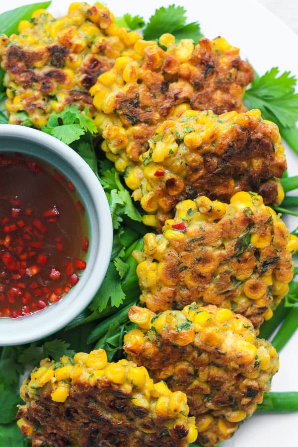 A plate of sweetcorn fritters on a table next to dipping sauce