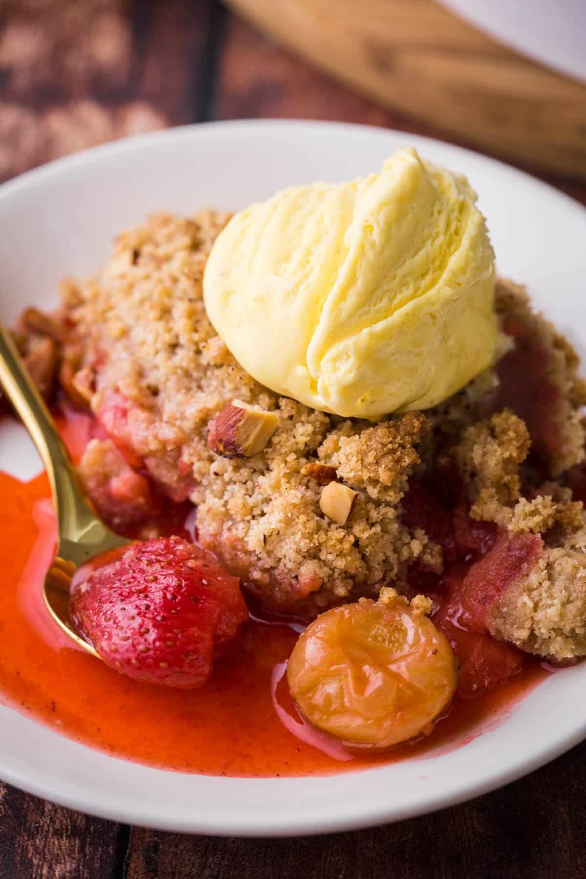 Overhead image of a bowl of Strawberry Gooseberry Crumble with ice cream and a spoon