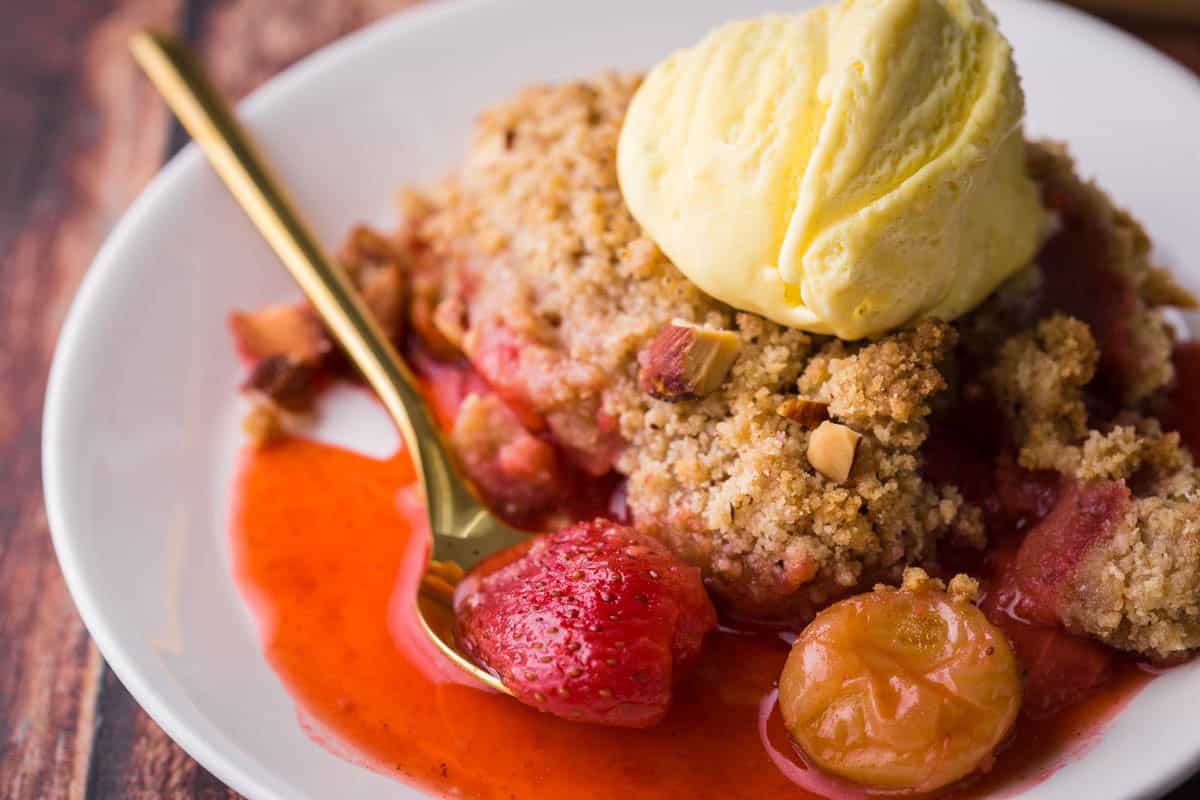 Overhead image of a bowl of Strawberry Gooseberry Crumble with ice cream and a spoon