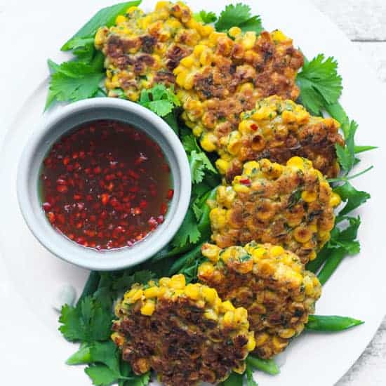 A plate of sweetcorn fritters on a table next to dipping sauce