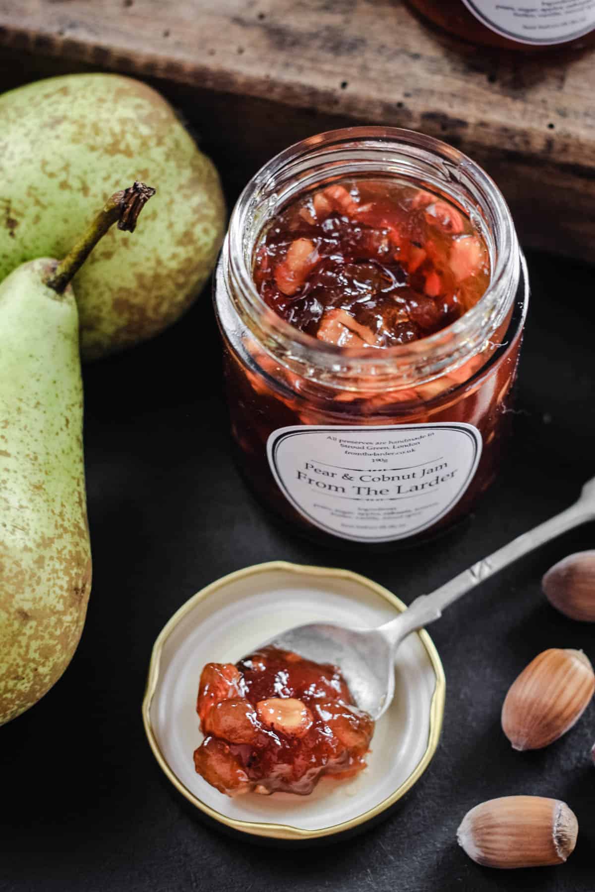 jar of jam next to pears and a spoon with jam resting on the lid