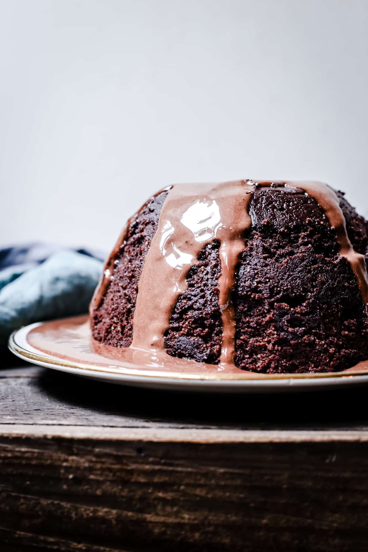 A whole Steamed Chocolate Sponge Pudding covered with Chocolate Custard on a plate on a wooden table