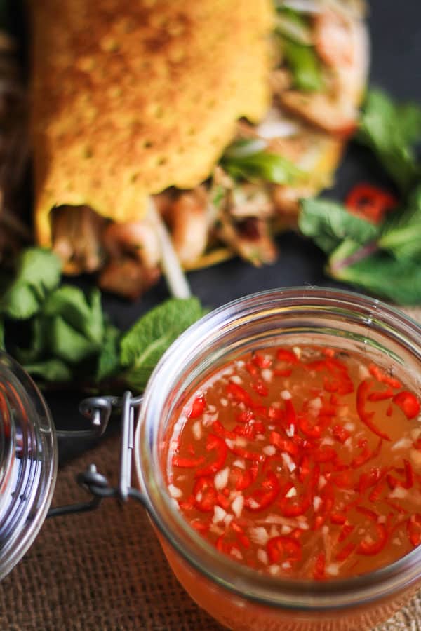 A bowl of dipping sauce and a banh xeo on a plate