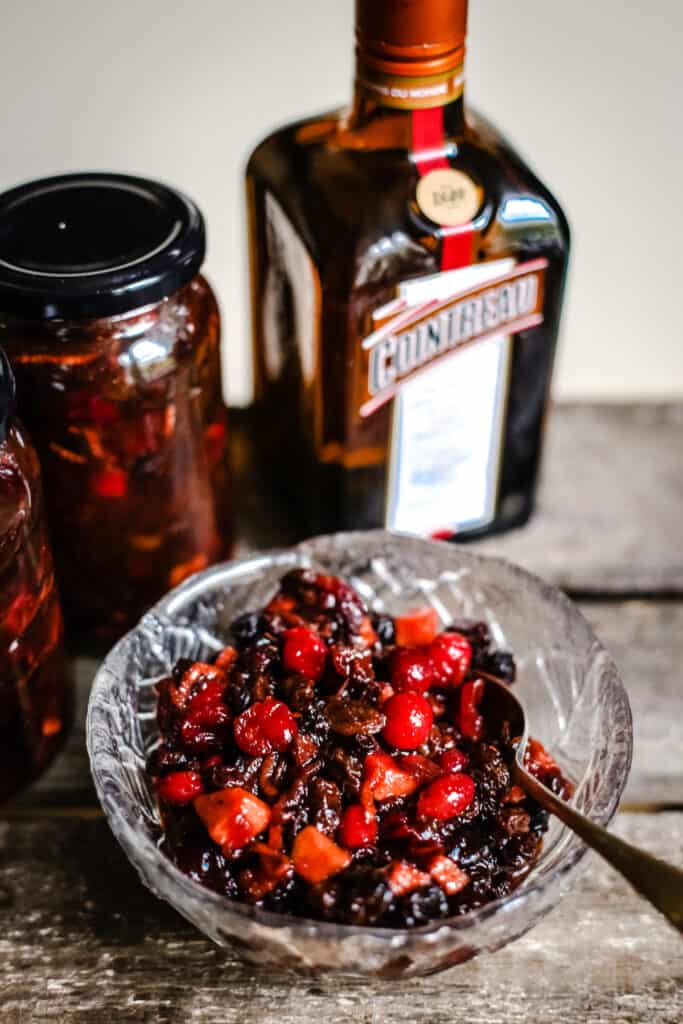 Cranberry Cointreau Mincemeat in a glass bowl next to jars of mincemeat and a bottle of cointreau on a wooden box