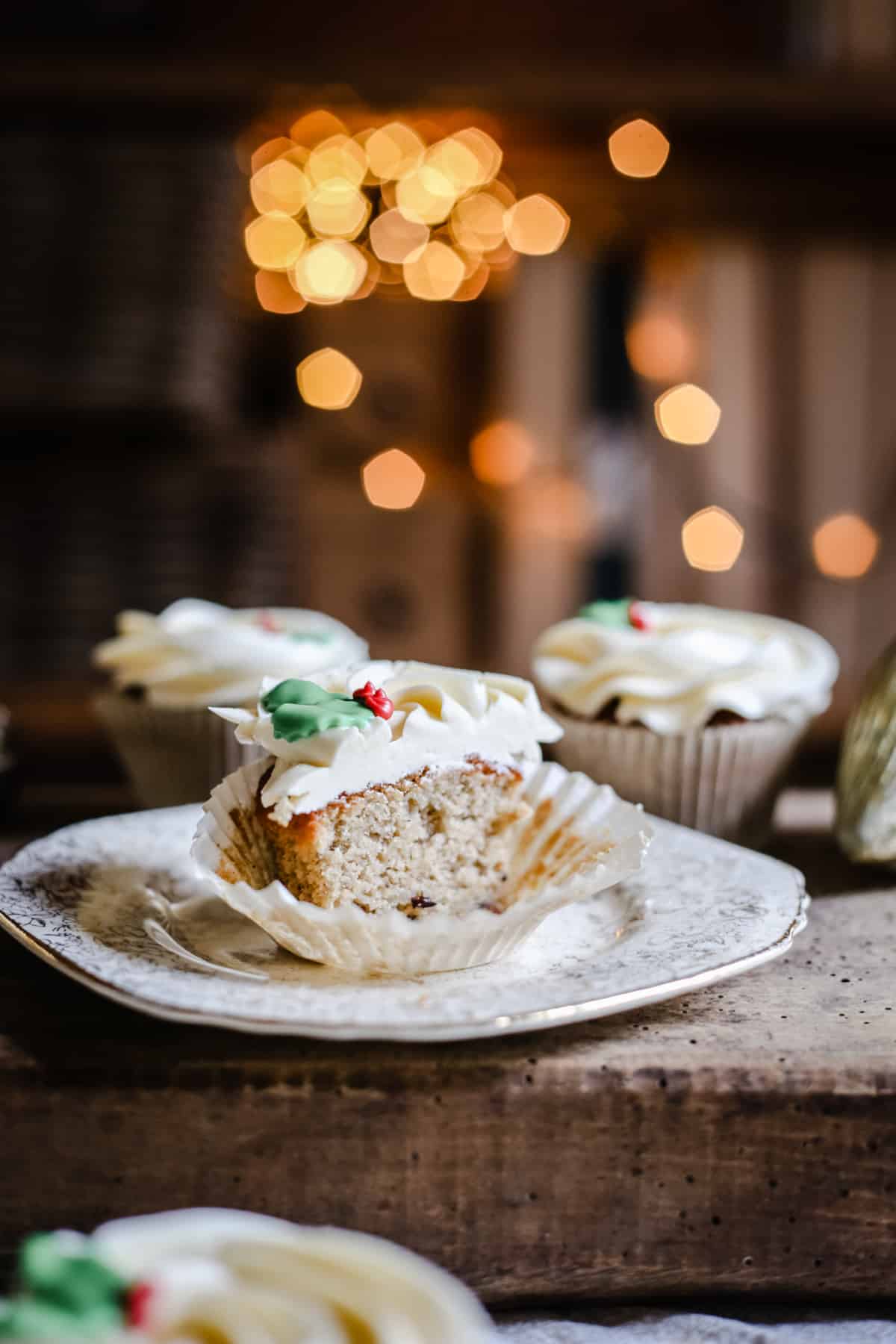 Mince Pie Cupcakes, sliced in half on a plate on a wooden board surrounded by cupcakes and twinkling lights