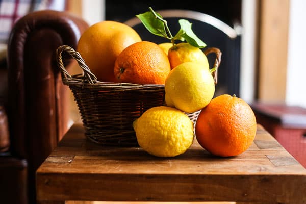 Oranges, lemons and grapefruit in or next to a basket on a wooden table