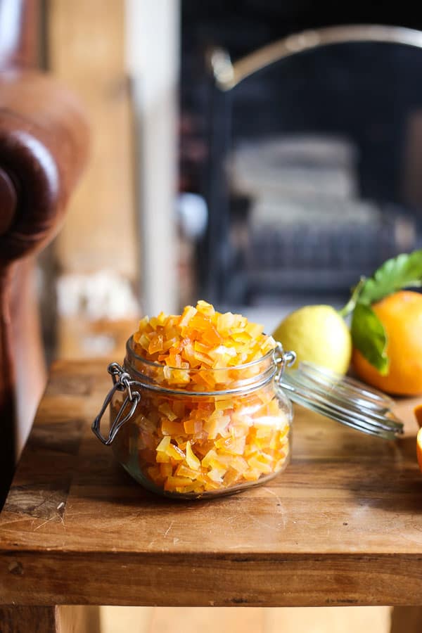 Homemade Mixed Peel in a jar on a wooden table surrounded by citrus fruits