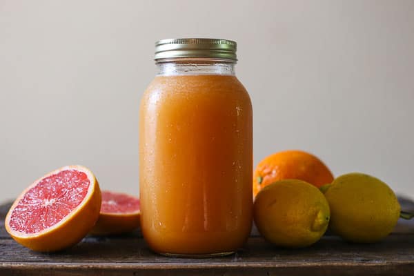 A jar of shrub surrounded by citrus fruit